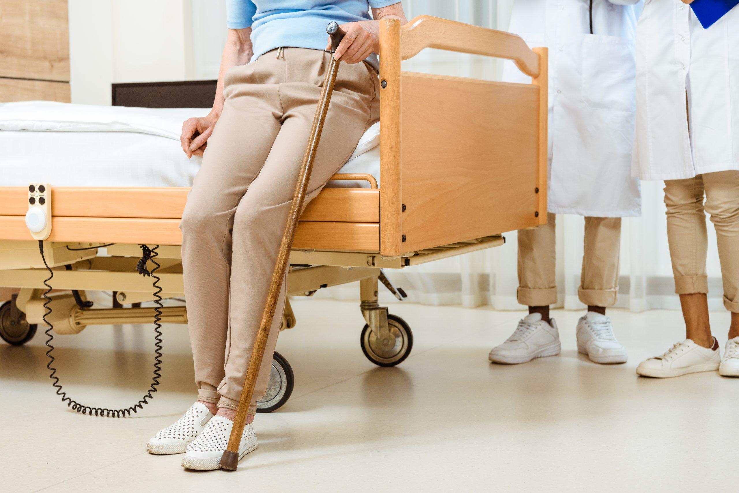 partial view of elderly woman with cane sitting on a hospital bed