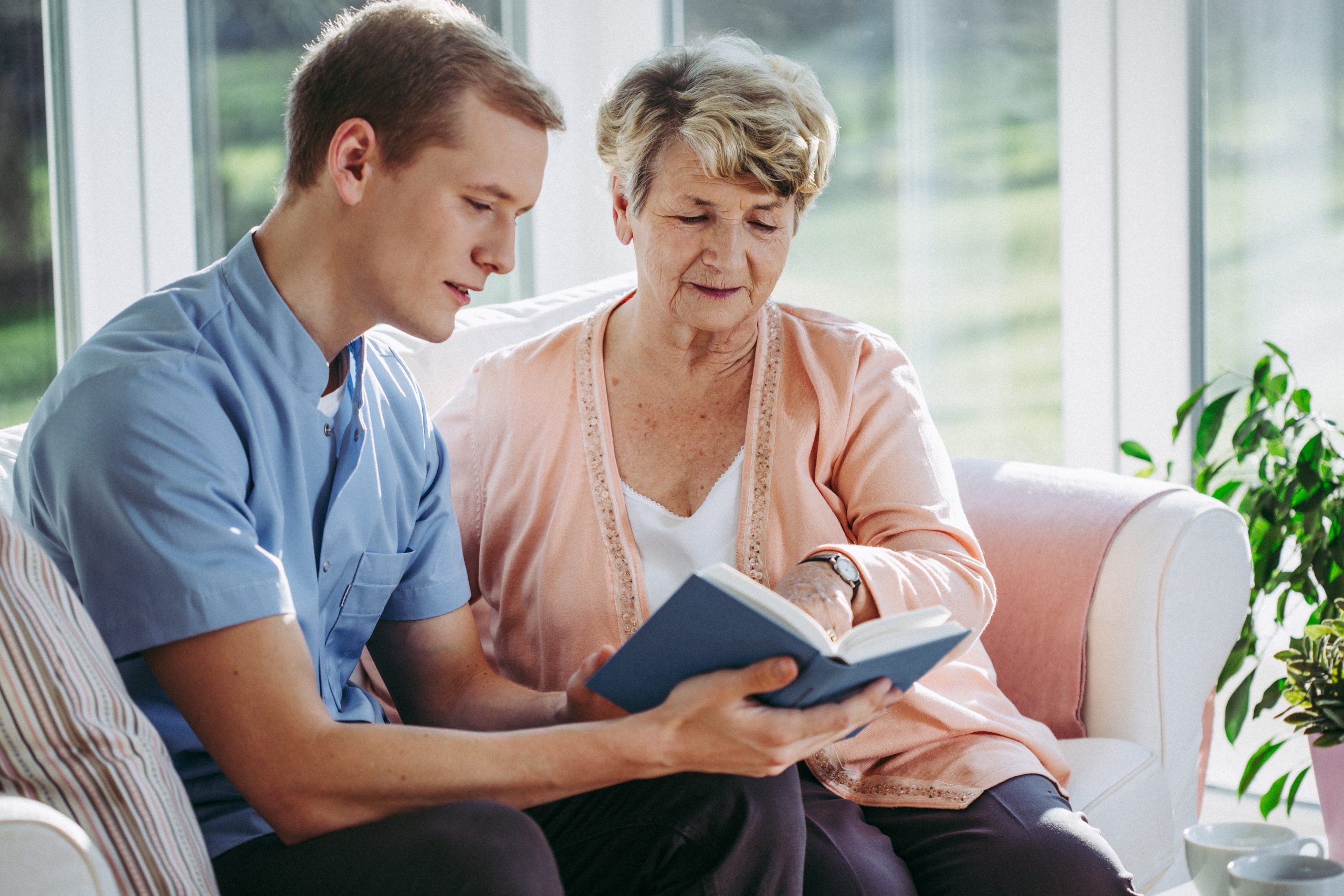 Senior woman and her male nurse reading a book together
