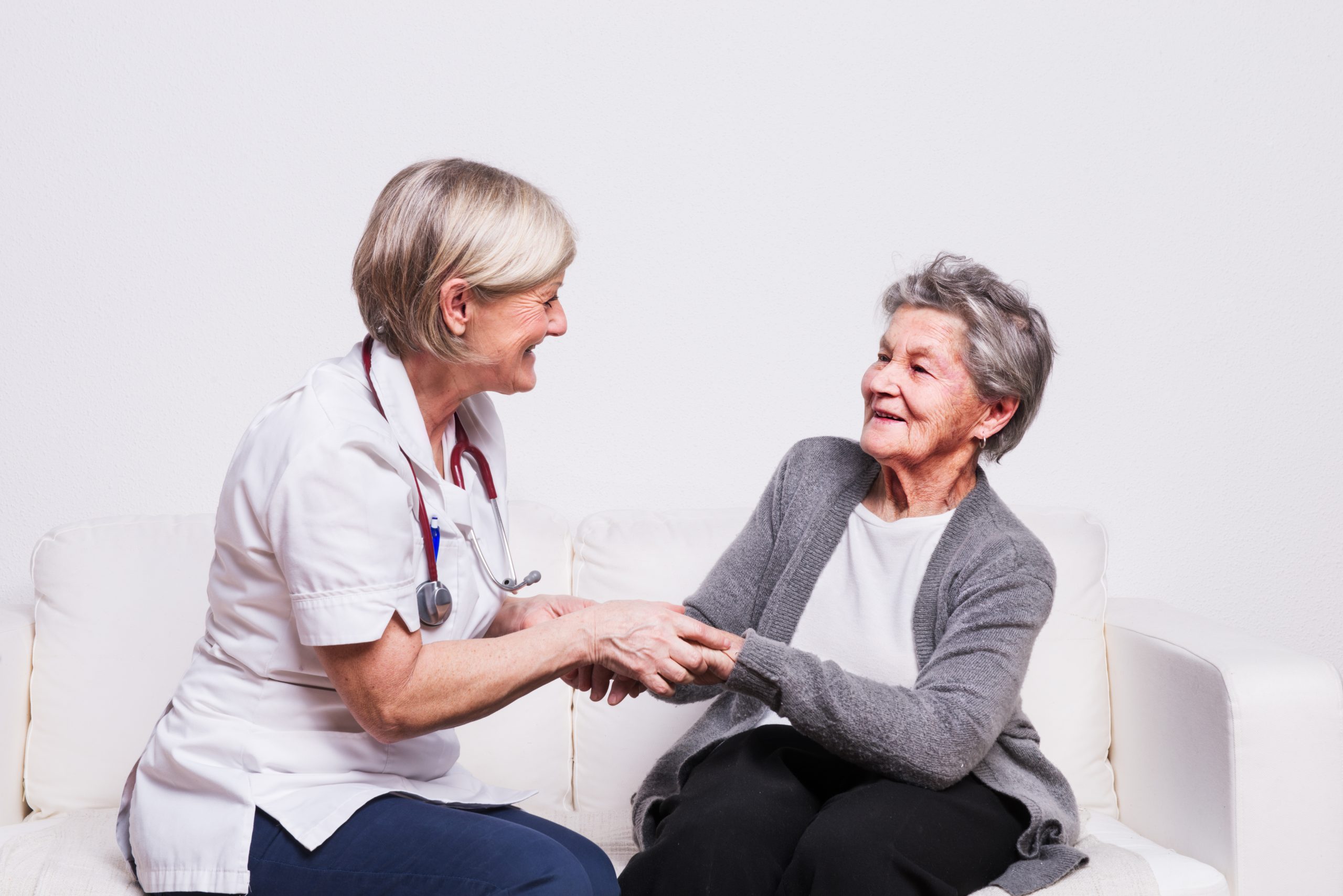 Studio portrait of a senior nurse and an elderly patient. Two women talking, holding hands.
