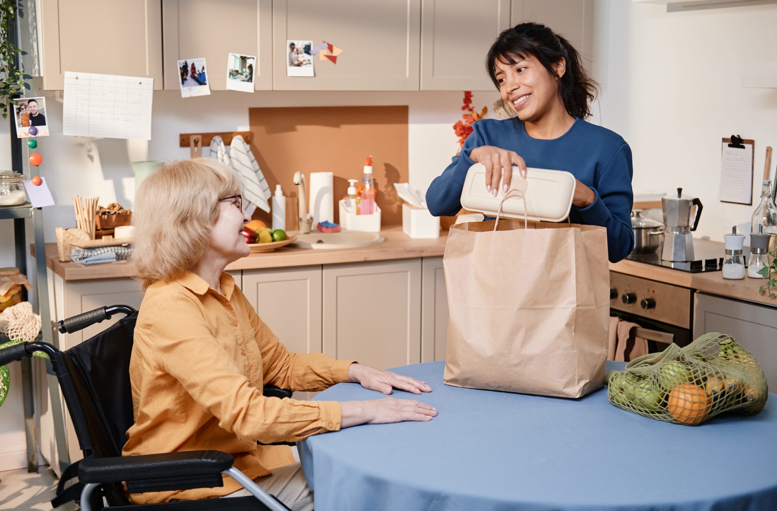 Smiling woman taking the food out of the paper bag at the table in the kitchen, she delivering food for senior woman